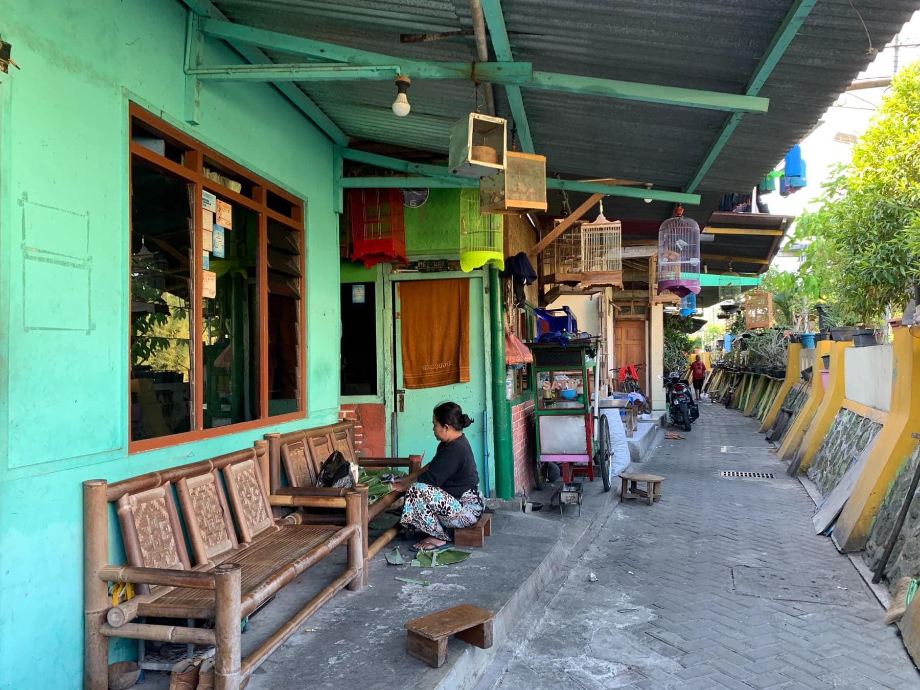 A person sitting beside a green-painted home along a narrow residential alley.