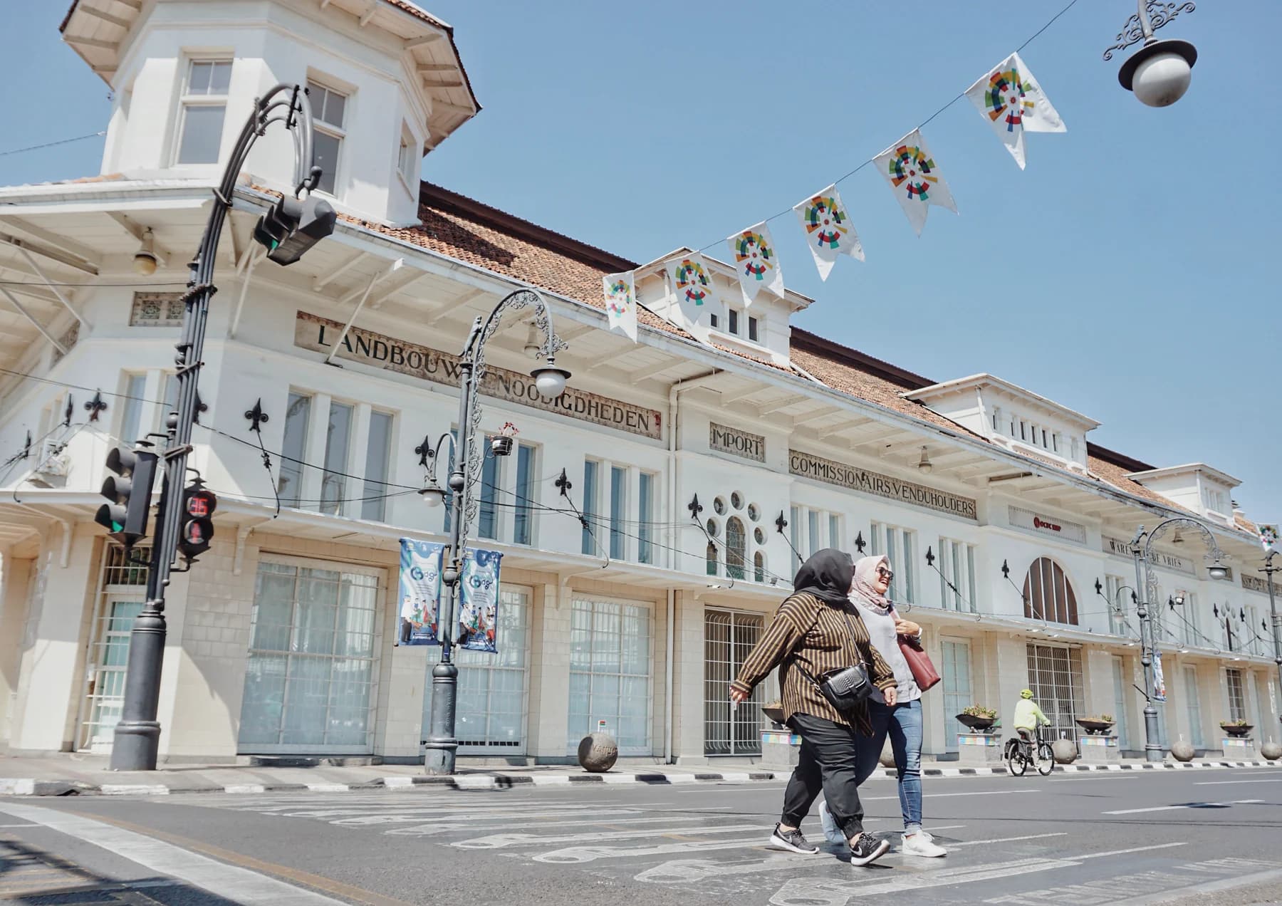 Two pedestrians crossing a street in front of a white heritage building.