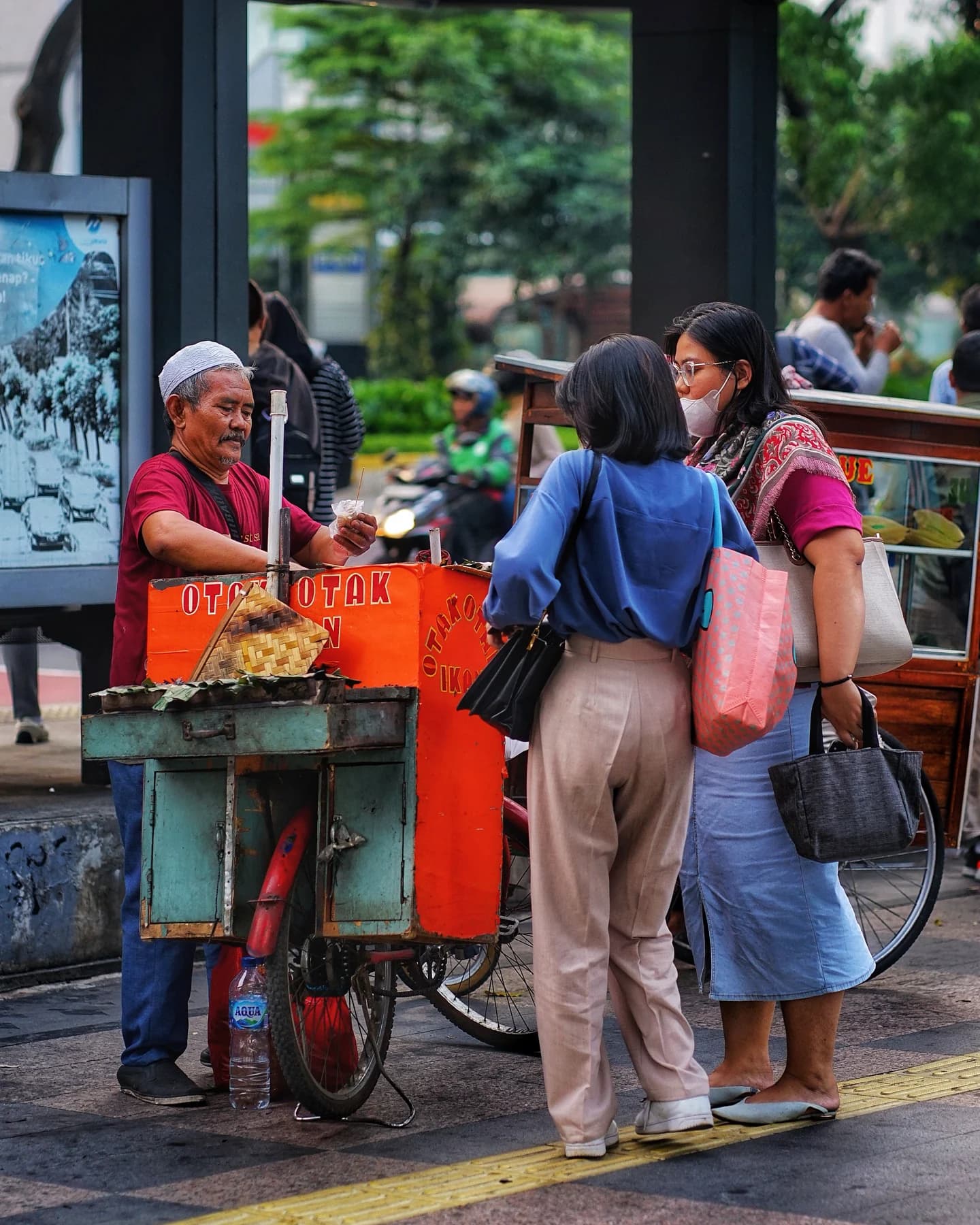 A smiling street vendor talking with customers beside a small food cart.